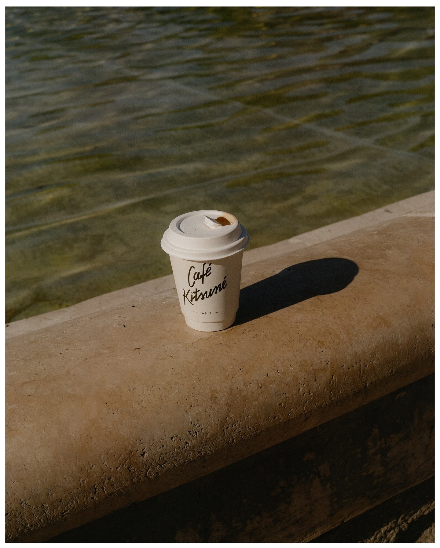 A paper coffee cup on a stone ledge above still green water