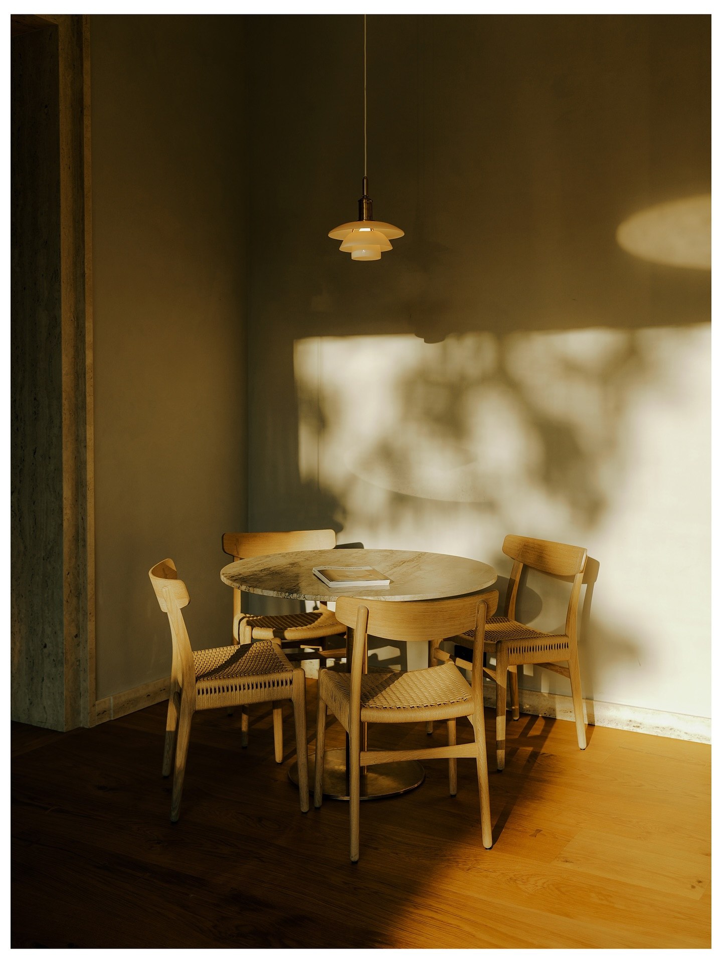 A round marble table and four chairs under a pendant lamp in late afternoon light