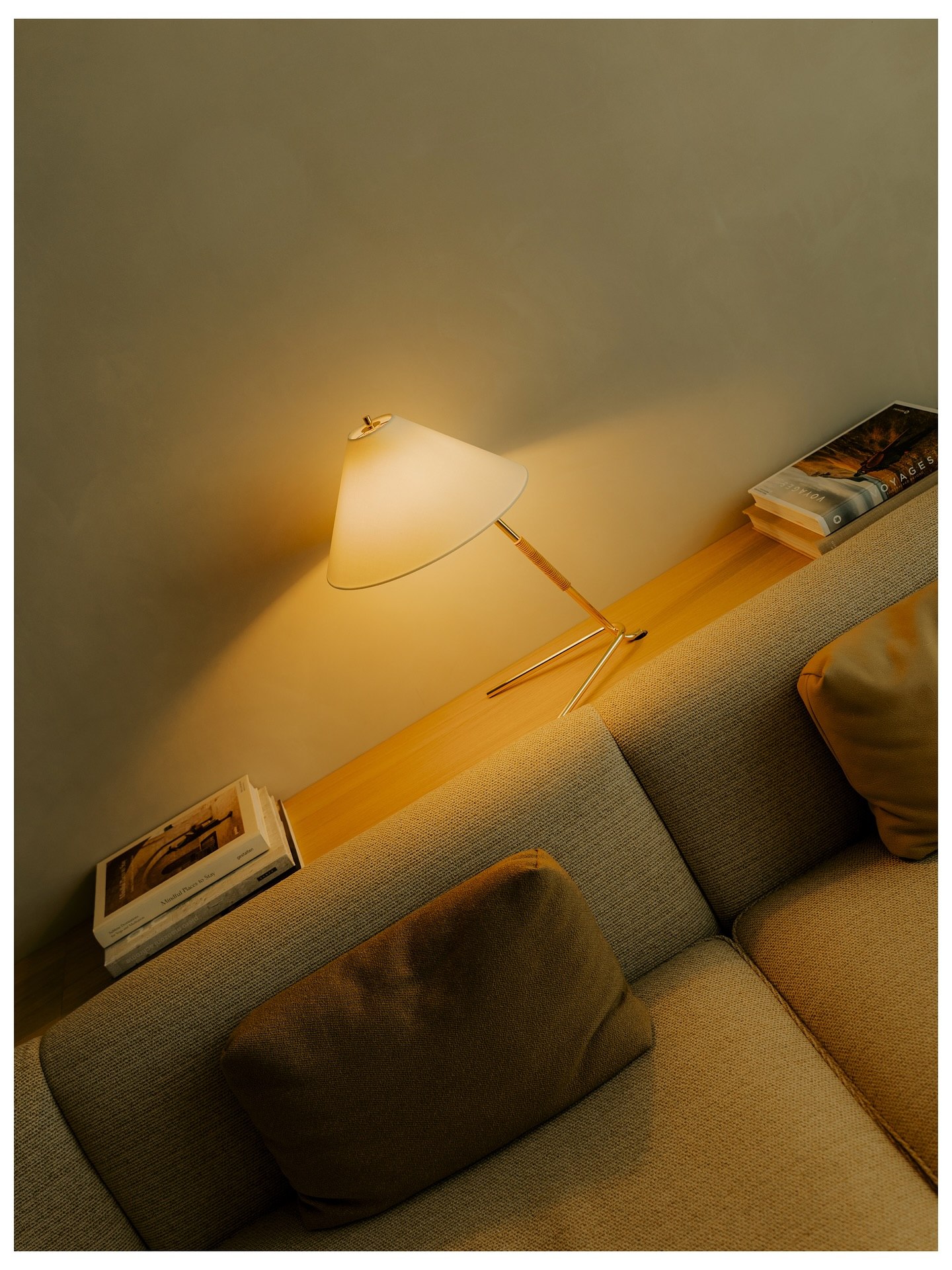 A brass lamp lit over a linen sofa, with travel books stacked on the ledge behind it
