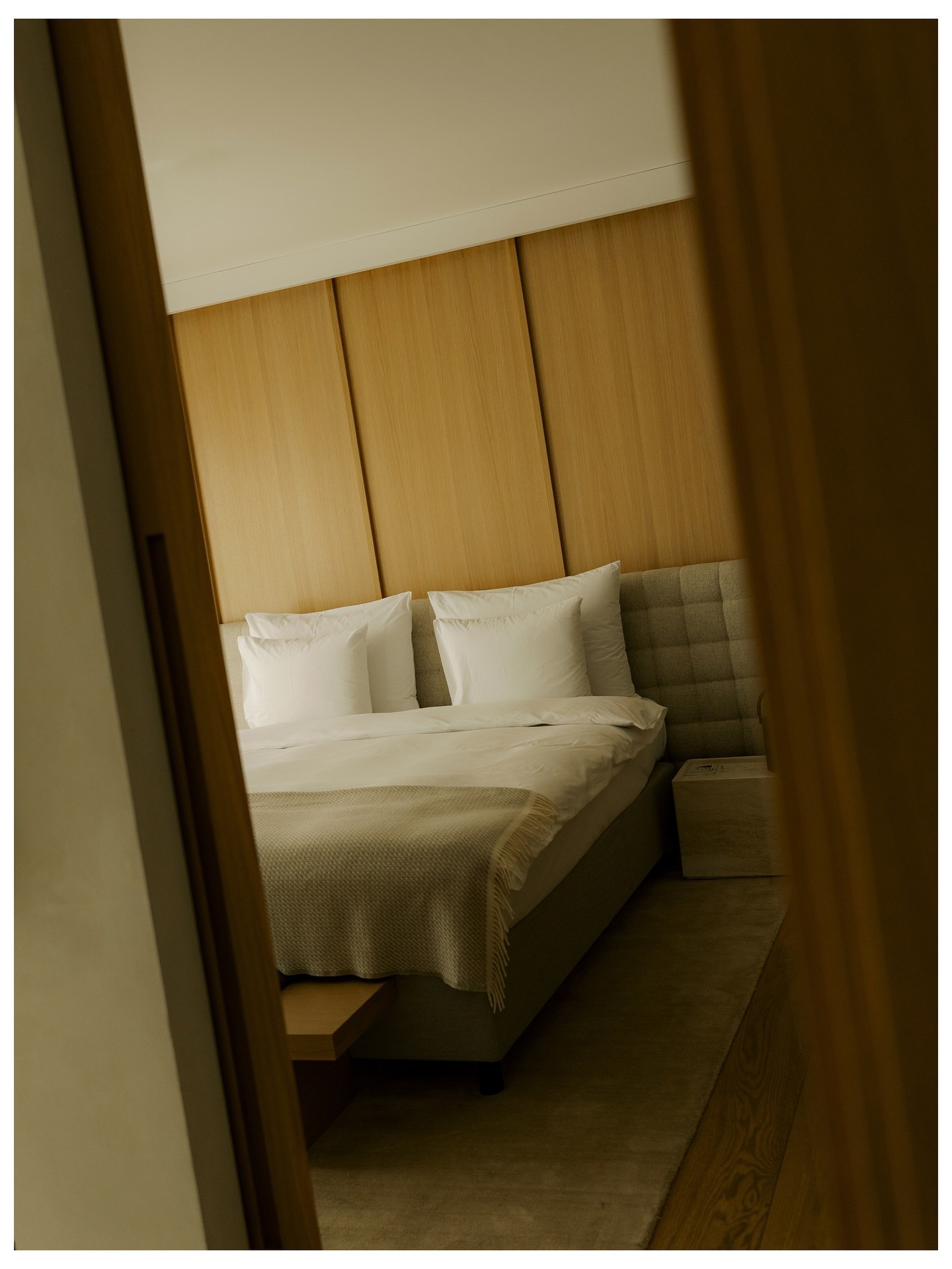 A made bed with white linen against an oak headboard, seen through a doorway