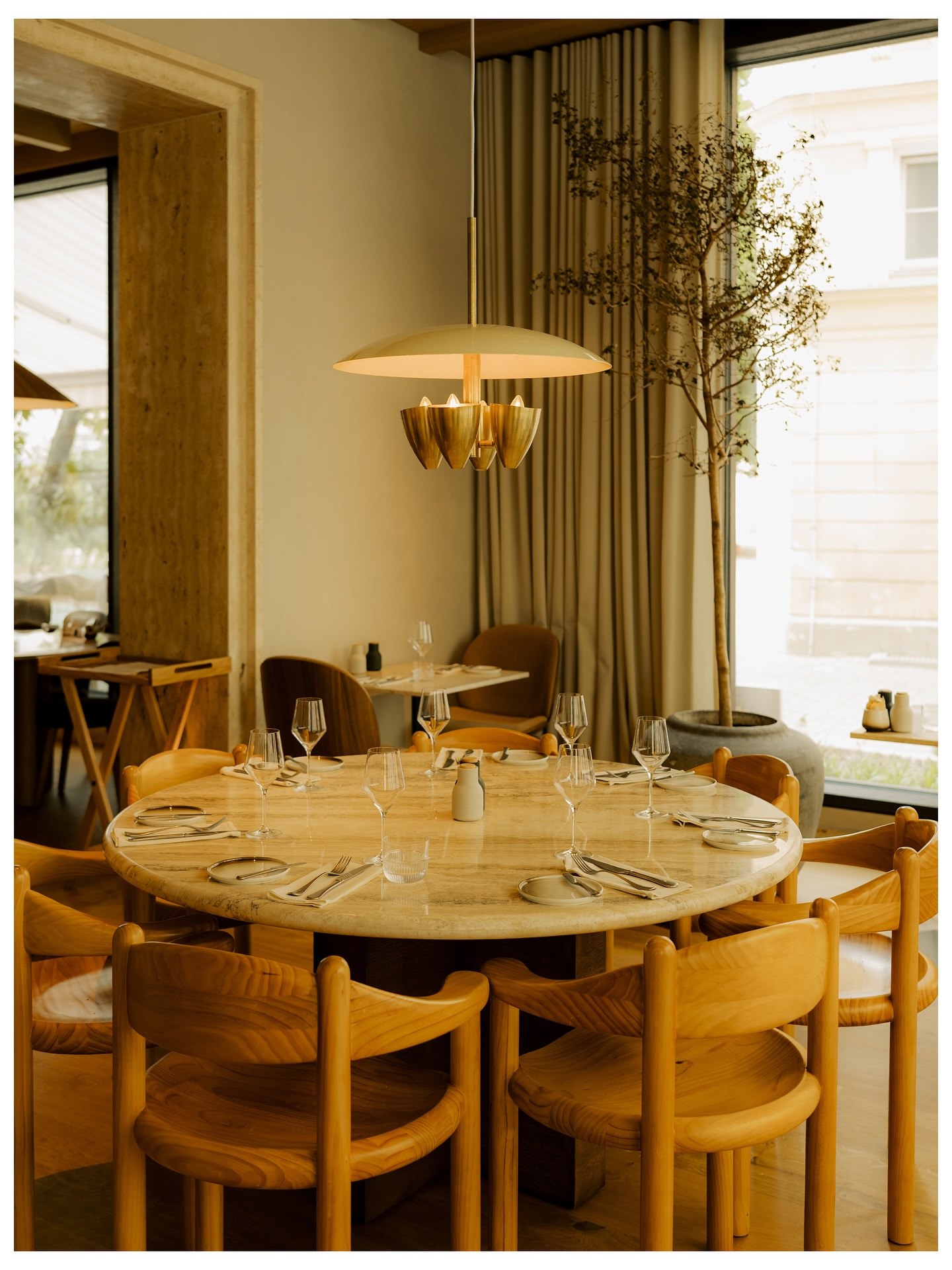 A laid round table under a brass pendant in a sunlit dining room